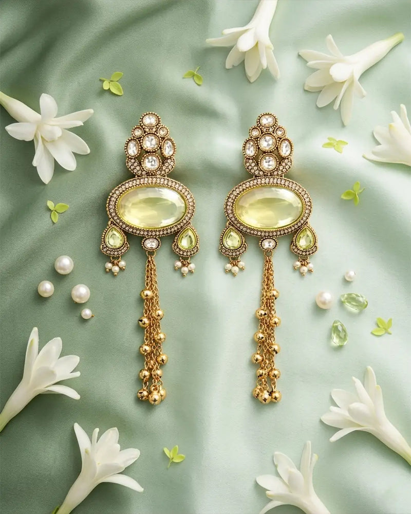 Ornate gold earrings with green gemstones on a light green background with white flowers.