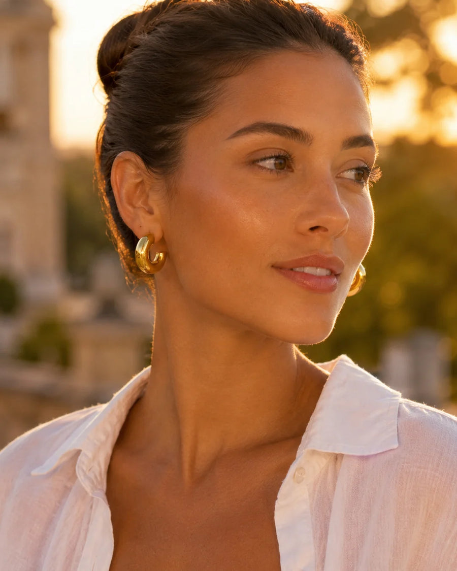 Woman wearing gold earrings with a blurred outdoor background
