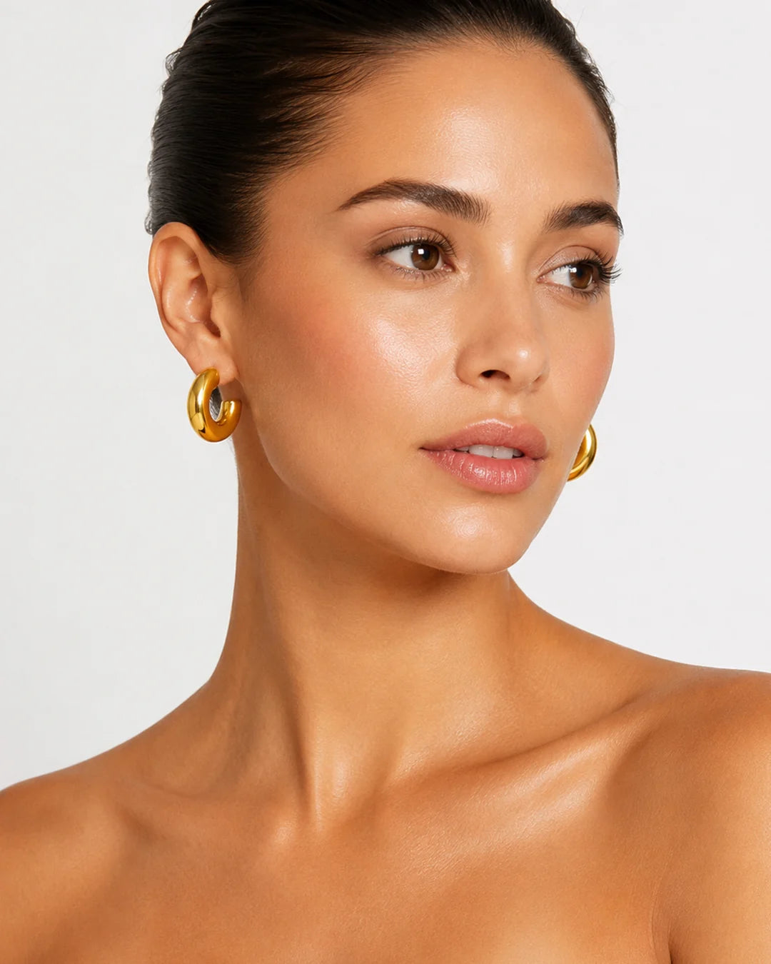Woman wearing gold hoop earrings against a neutral background
