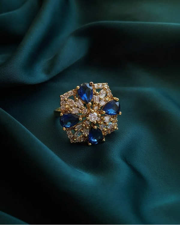 Elegant ring with blue gemstones and gold accents on a teal fabric background