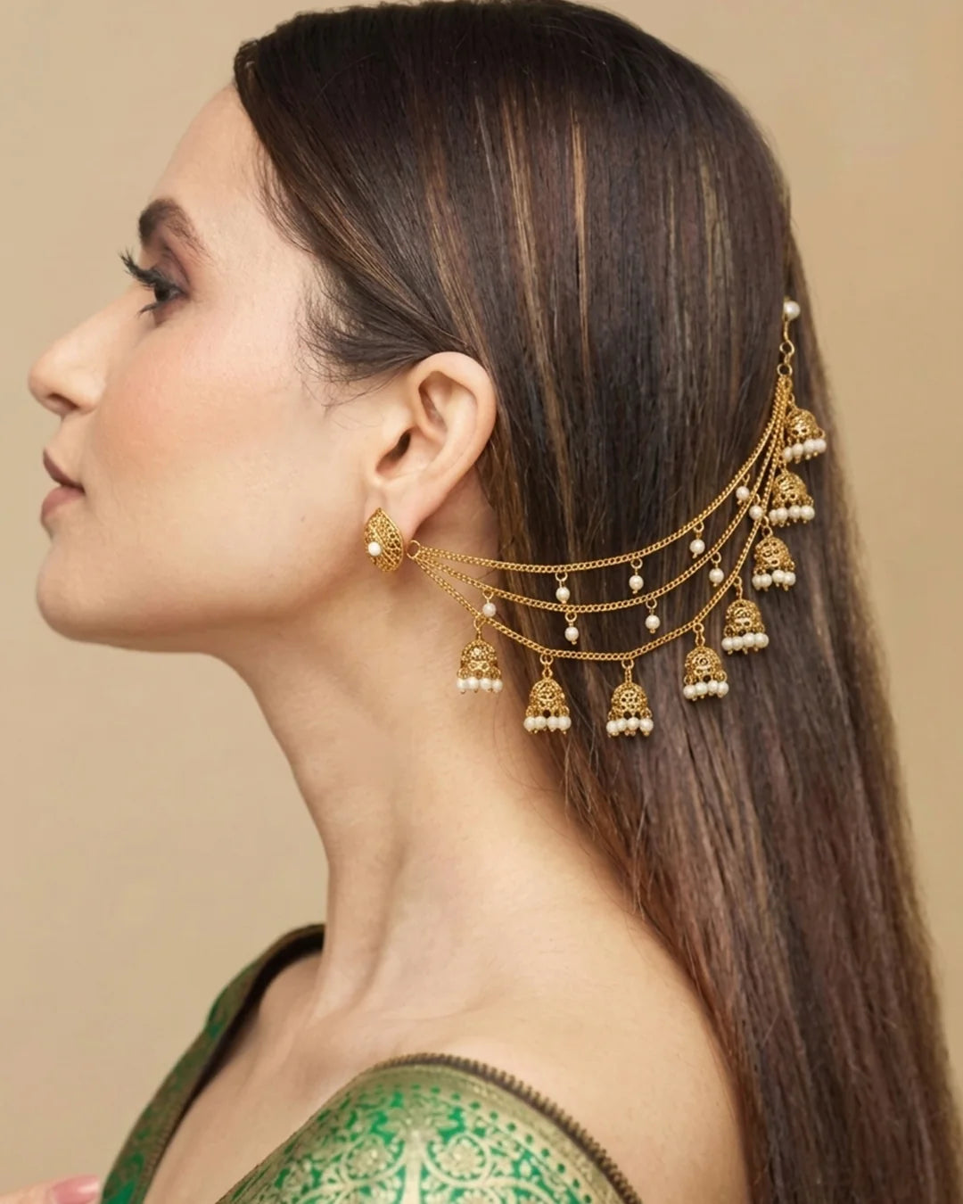 Woman wearing a gold hair accessory with dangling elements on a beige background