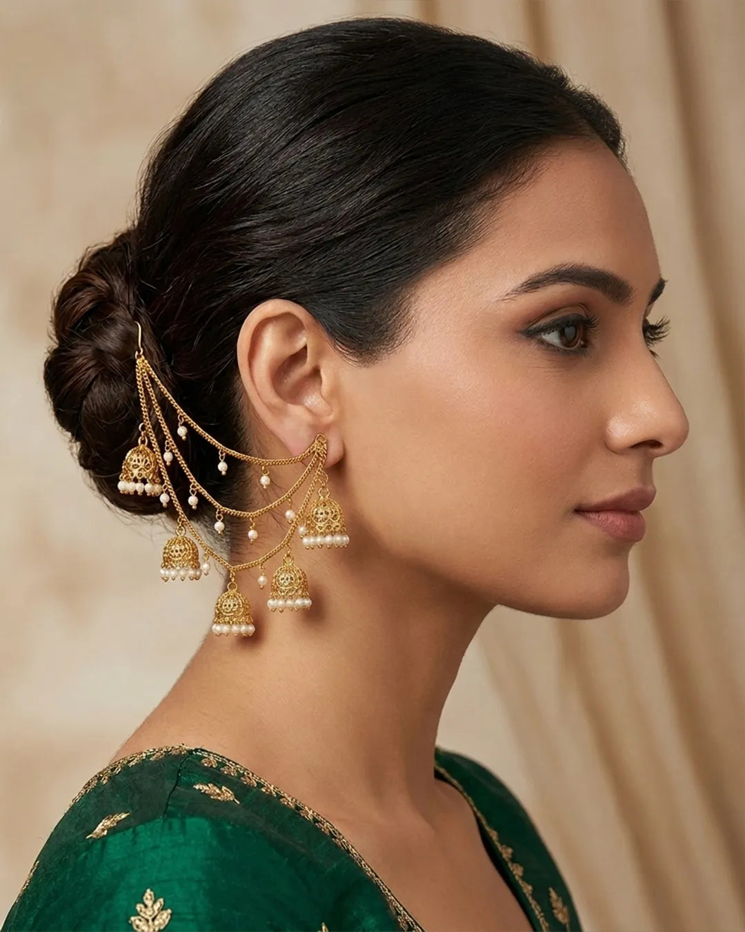 Woman wearing gold earrings with dangling beads against a beige background