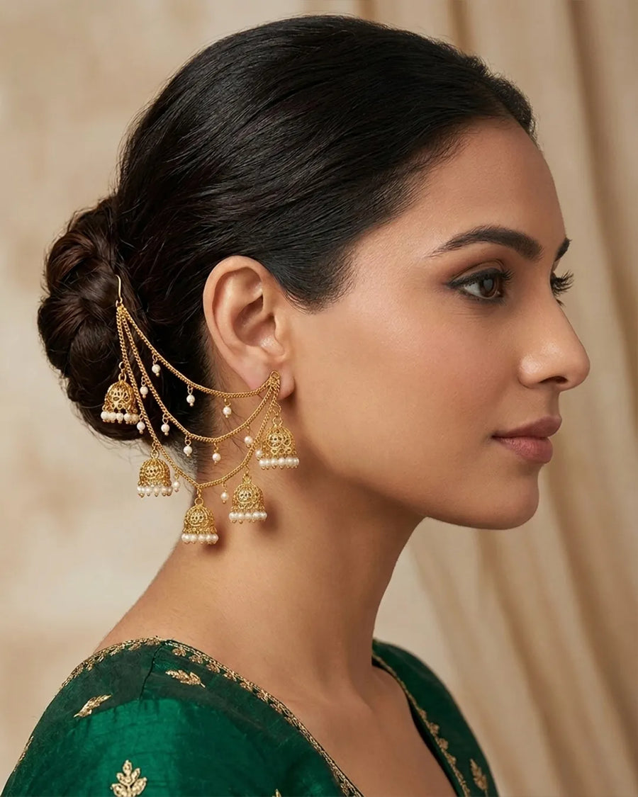 Woman wearing gold earrings with dangling beads against a beige background