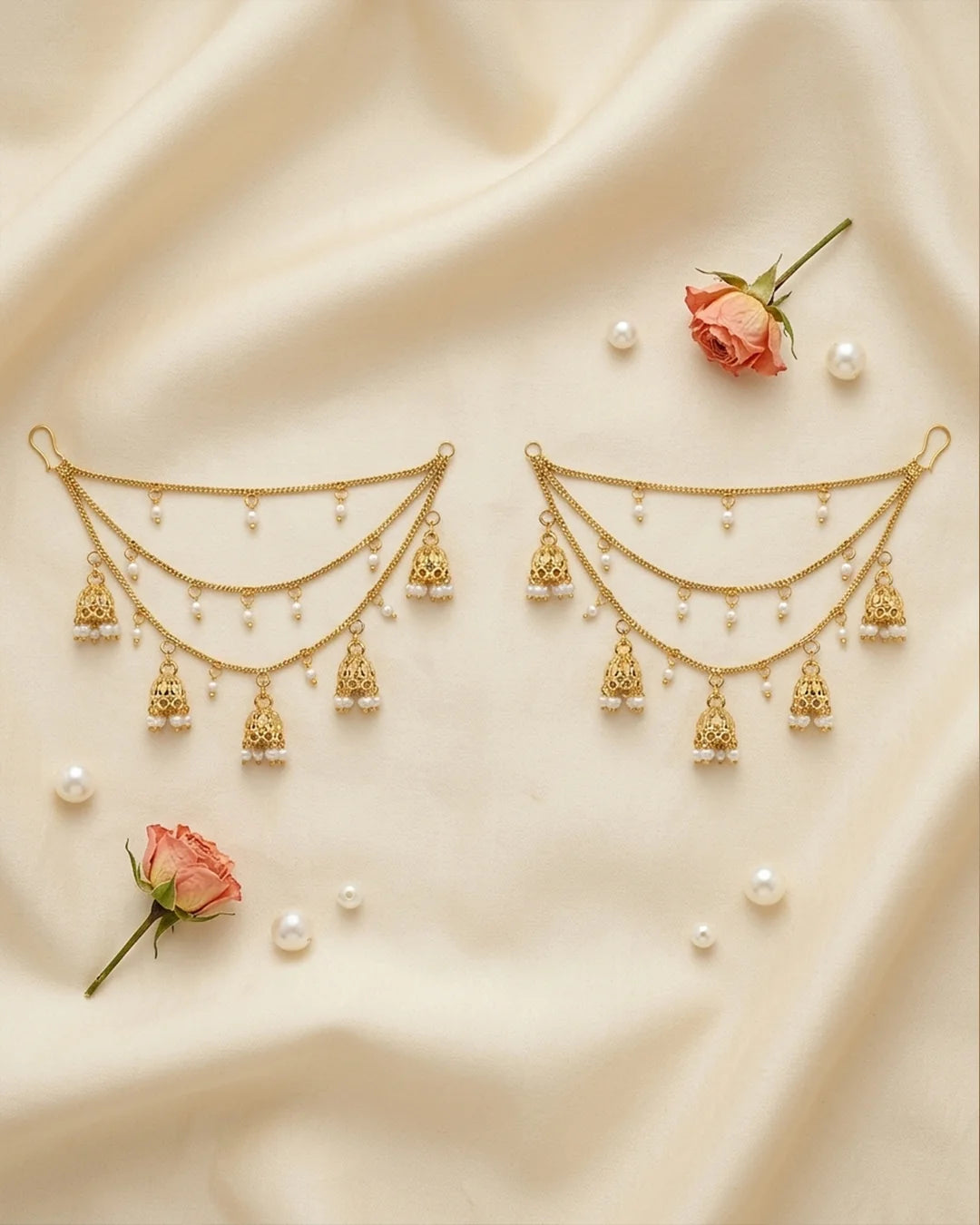 Pair of gold earrings with hanging charms on a beige fabric background with small pink roses and pearls.