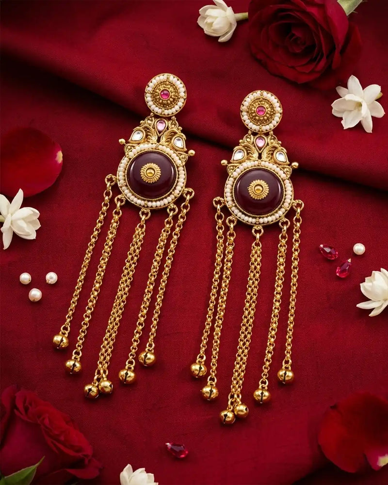 Ornate gold earrings with maroon centers on a red fabric background with flowers.
