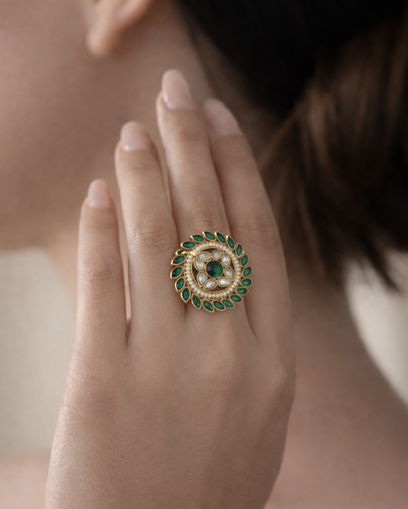 Close-up of a hand wearing an ornate ring with green gemstones and pearls.