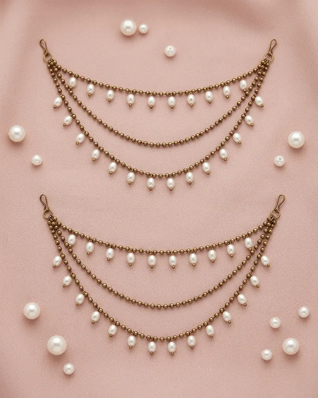 Two pearl and bronze ear chains on a pink background with scattered pearls.