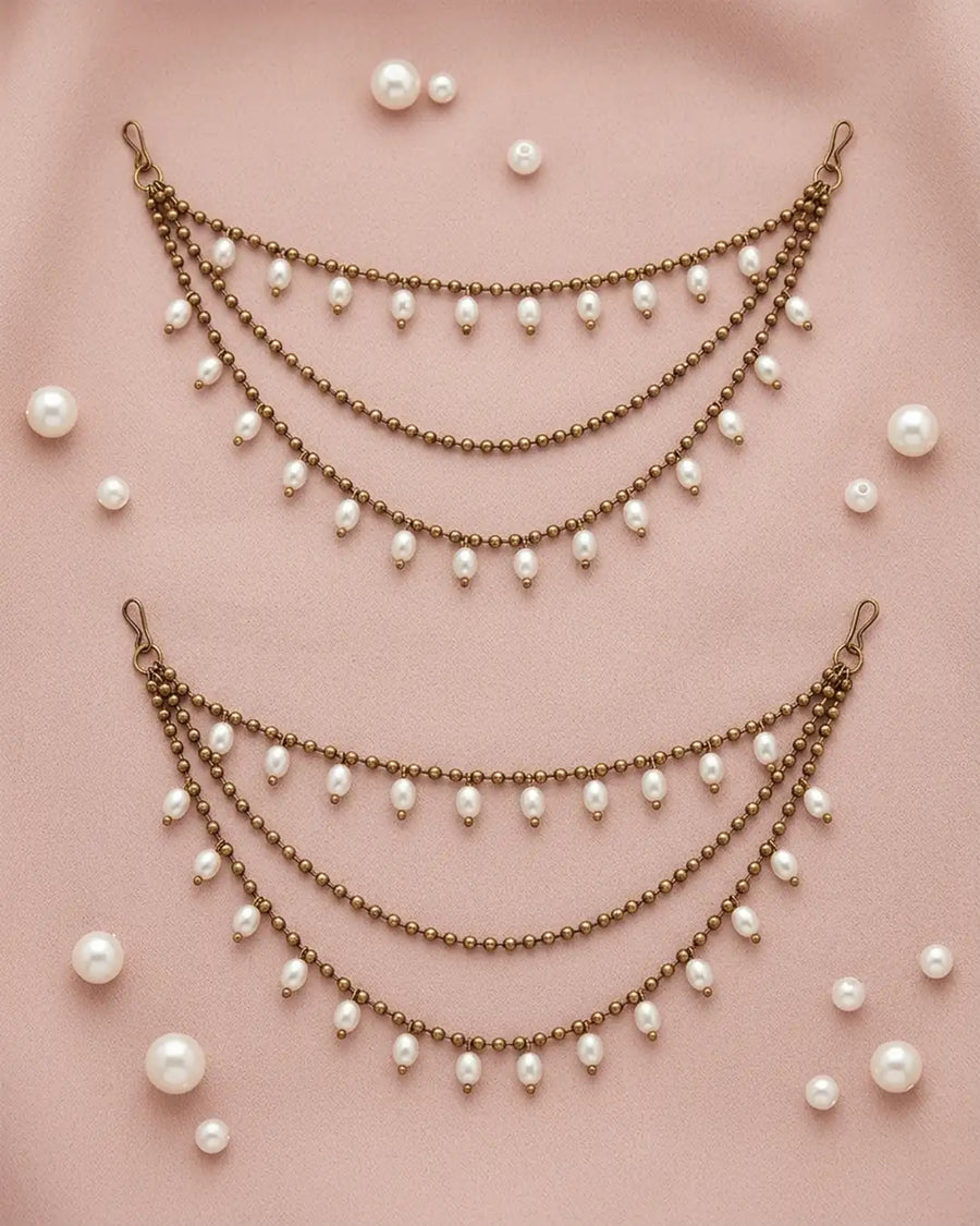 Two pearl and bronze ear chains on a pink background with scattered pearls.