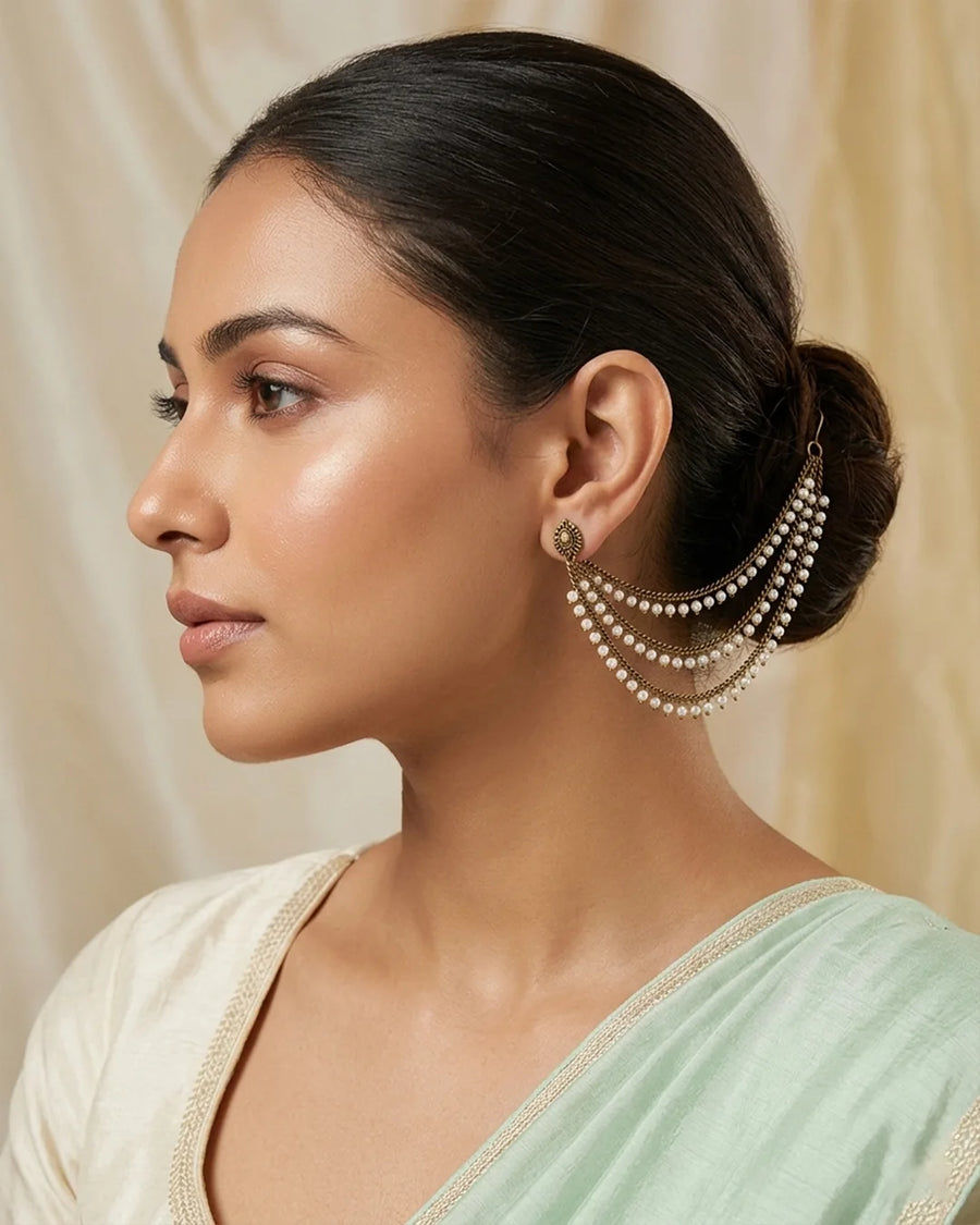 Woman wearing a light green saree with pearl earrings against a beige background