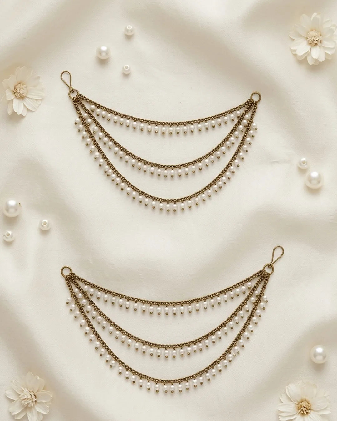 Two pearl and ear chains  on a soft beige fabric background with scattered pearls and flowers.