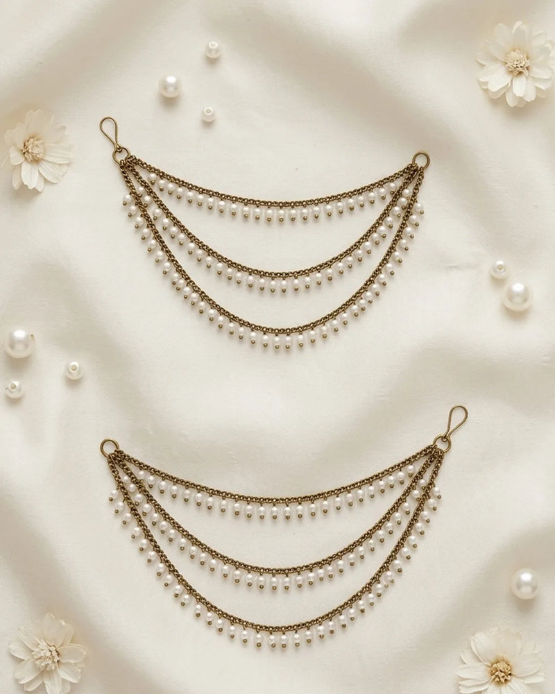 Two pearl and ear chains  on a soft beige fabric background with scattered pearls and flowers.