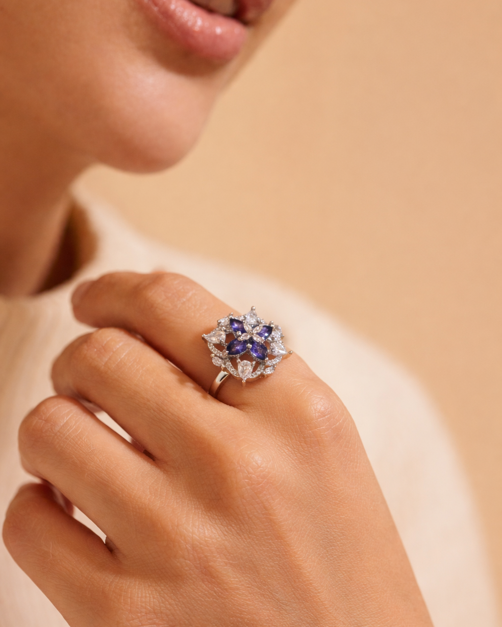 Close-up of a hand wearing a decorative ring with gemstones on a beige background