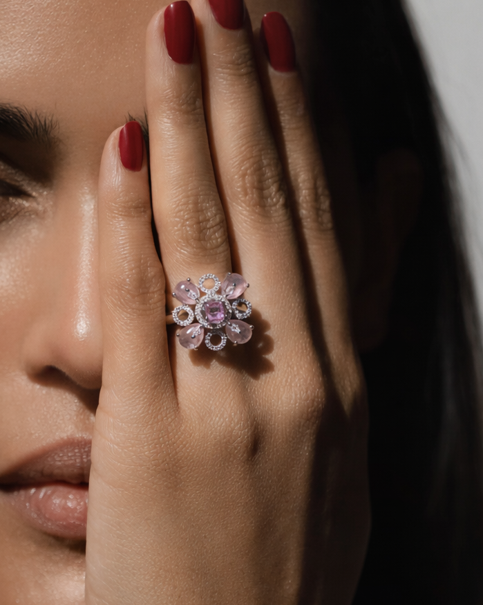 Close-up of a hand wearing a decorative ring with pink gemstones, held near the face.