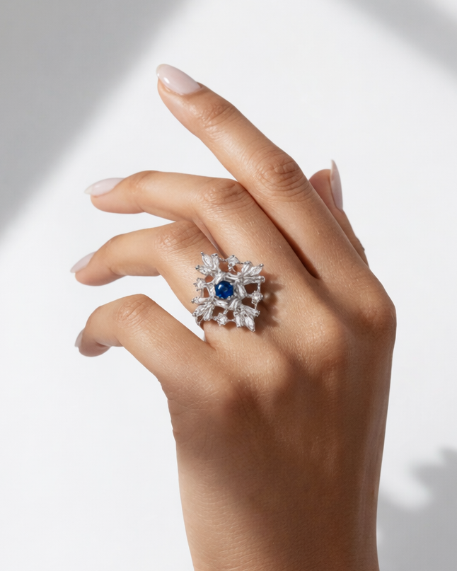 Hand wearing a decorative ring with a blue gemstone on a light background