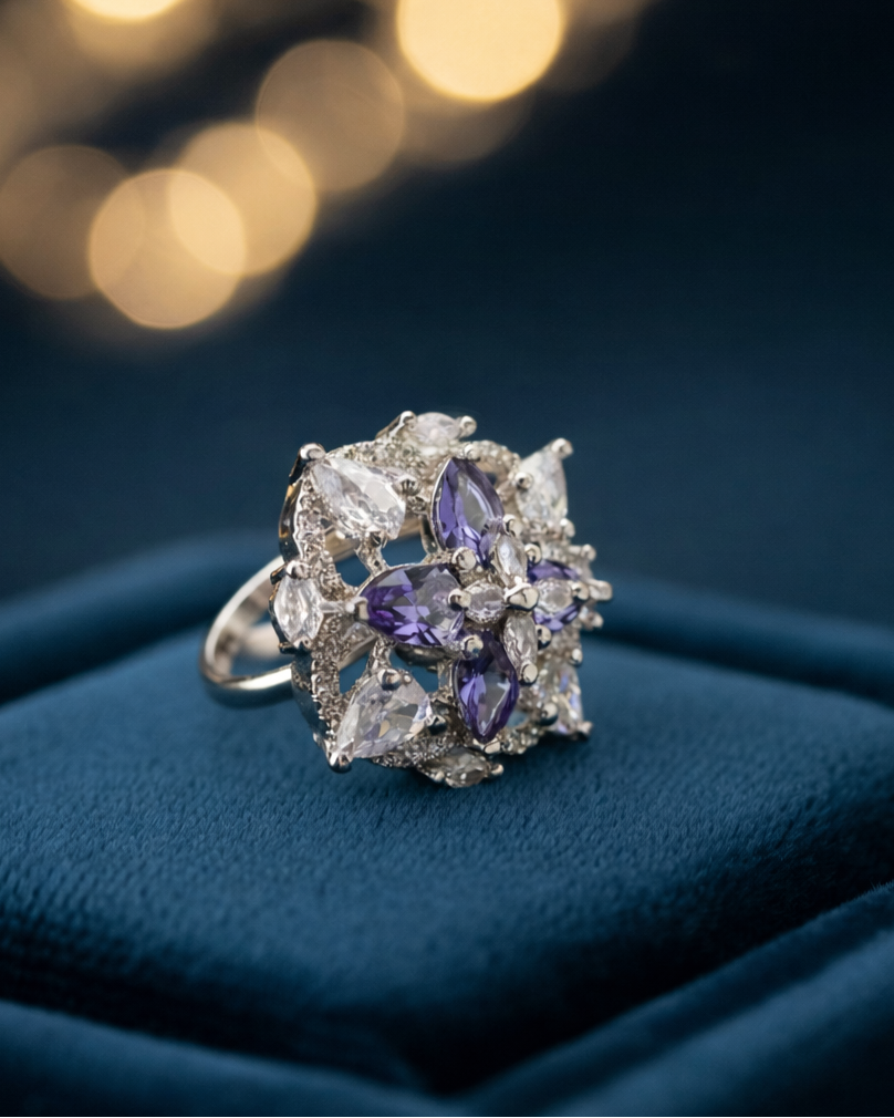Silver ring with purple gemstones on a blue cushion with blurred lights in the background