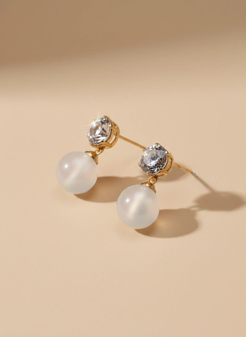 Pair of earrings with gold accents and clear gemstones on a beige background