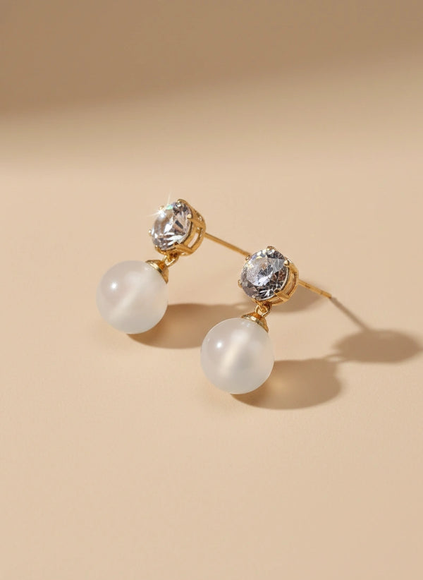 Pair of earrings with gold accents and clear gemstones on a beige background