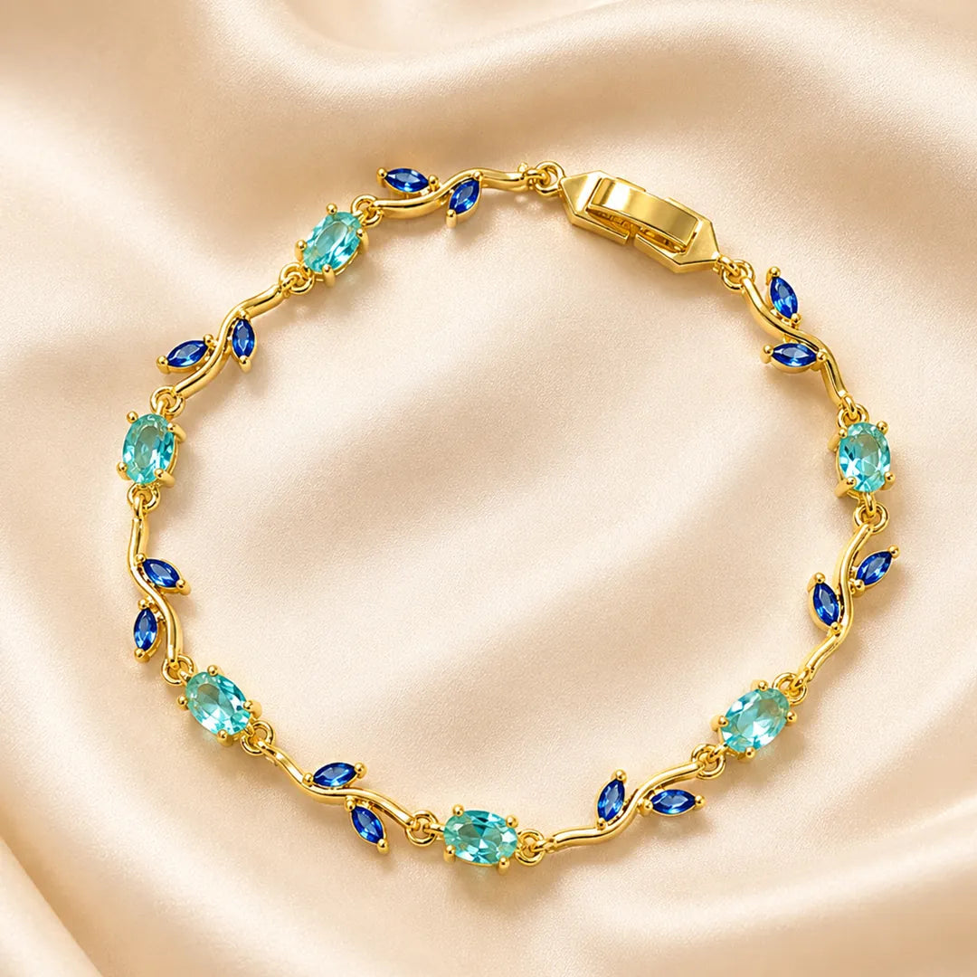 Gold bracelet with blue and green gemstones on a beige satin background